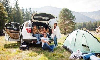 Glückliche Familie beim Camping in den Bergen, mit offenem Auto-Kofferraum und Zelt – eine gut geplante Reise mit Campingtoilette für mehr Komfort.