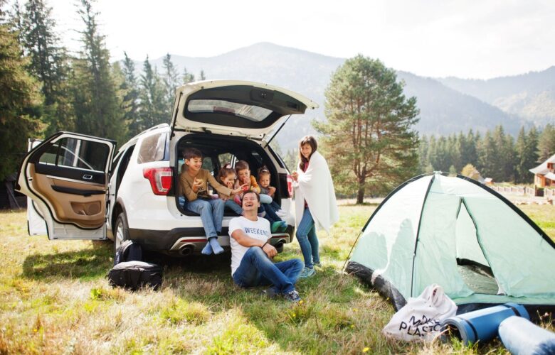 Glückliche Familie beim Camping in den Bergen, mit offenem Auto-Kofferraum und Zelt – eine gut geplante Reise mit Campingtoilette für mehr Komfort.