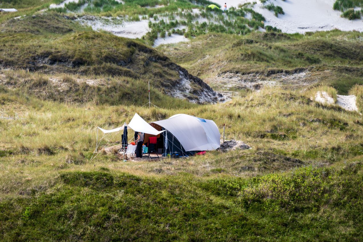 Großes Familienzelt steht mitten in den Dünen, umgeben von Gras und Sand – nachhaltiges Camping mit Campingtoilette für eine umweltfreundliche Reise.