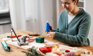 Winterurlaub, DIY und Hobby Konzept - Frau mit Heißklebepistole, die Adventskalender bastelt oder Weihnachtsgeschenk zu Hause verpackt