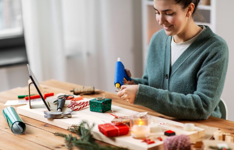 Winterurlaub, DIY und Hobby Konzept - Frau mit Heißklebepistole, die Adventskalender bastelt oder Weihnachtsgeschenk zu Hause verpackt