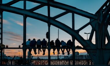 Klassenfahrt München: Jugendliche Gruppe sitzt auf Stahlbrücke in München bei Sonnenuntergang