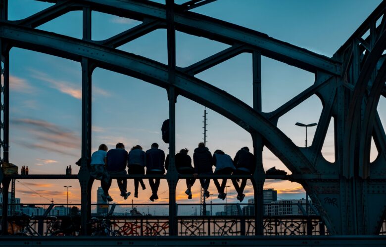 Klassenfahrt München: Jugendliche Gruppe sitzt auf Stahlbrücke in München bei Sonnenuntergang
