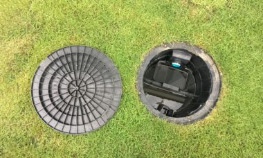 Geöffneter Abdeckung eines Abwassertanks im Garten mit schwarzem Kunststoffdeckel auf Rasen