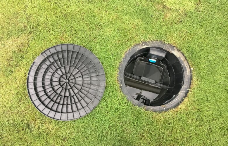 Geöffneter Abdeckung eines Abwassertanks im Garten mit schwarzem Kunststoffdeckel auf Rasen